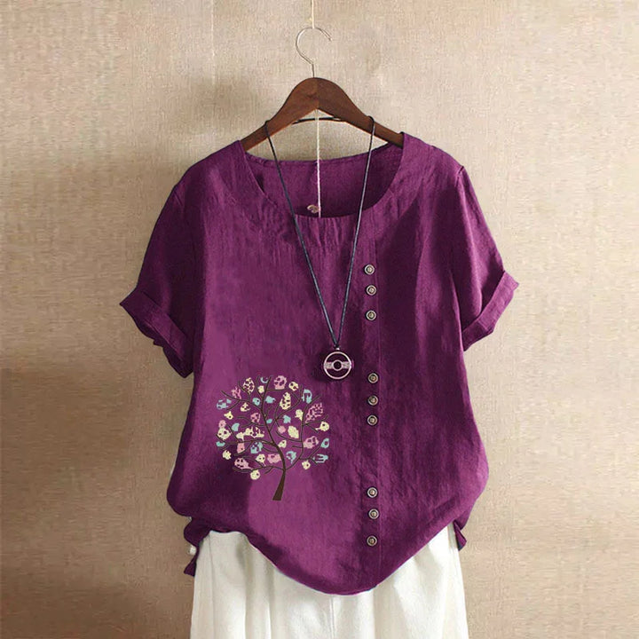 Purple short-sleeve blouse with button details and tree print, paired with white skirt on wooden hanger
