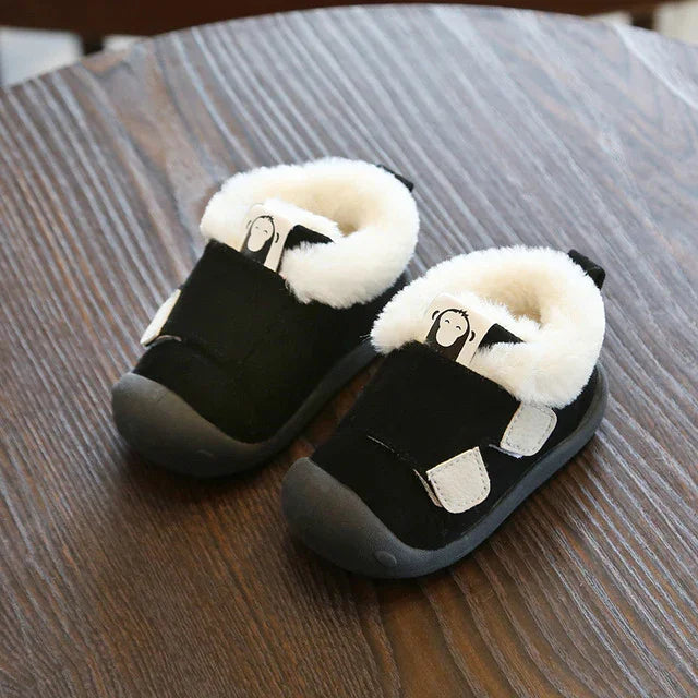 Black toddler shoes with white fluffy lining and velcro straps on wooden surface
