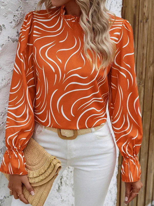 Woman wearing an orange and white abstract print blouse with puffed sleeves, white pants, and holding a woven clutch