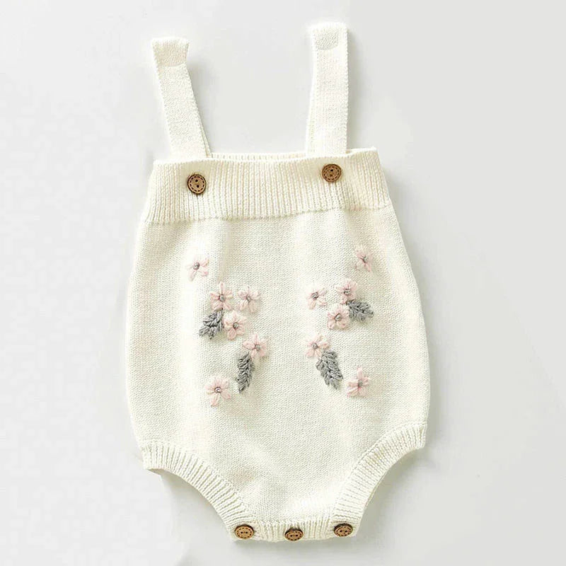 White knitted baby romper with floral embroidery, button straps, and bottom buttons
