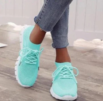 close-up of person wearing mint green knit sneakers with white soles on wooden floor