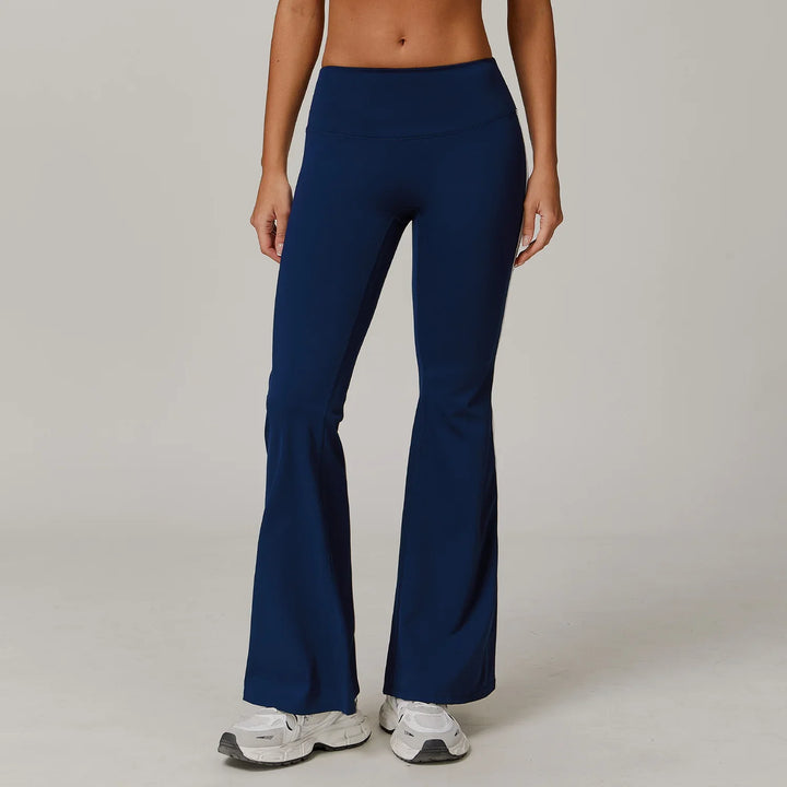 Model wearing navy blue high-waisted flare leggings with white sneakers on gray background
