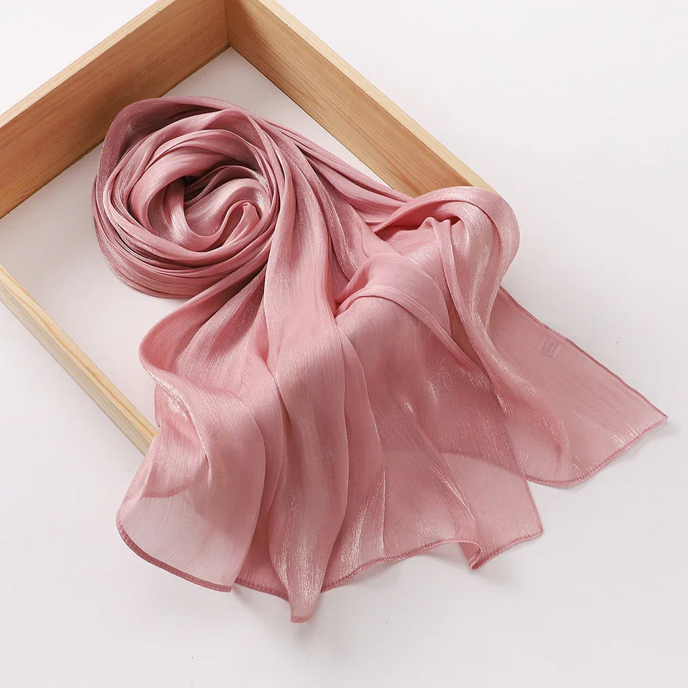 Soft shimmering pink silk scarf elegantly arranged in a light wooden tray on white surface