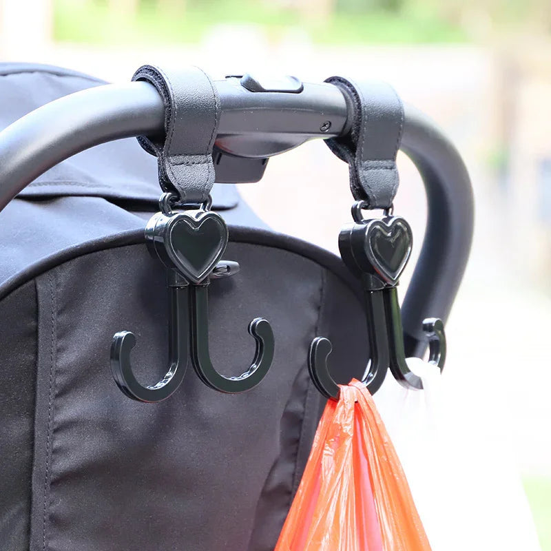 Black heart-shaped double hooks hanging on stroller handle holding a pink plastic bag
