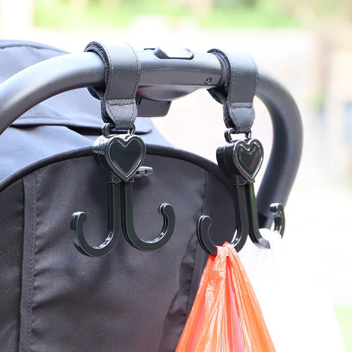 Black heart-shaped double hooks hanging on stroller handle holding a pink plastic bag
