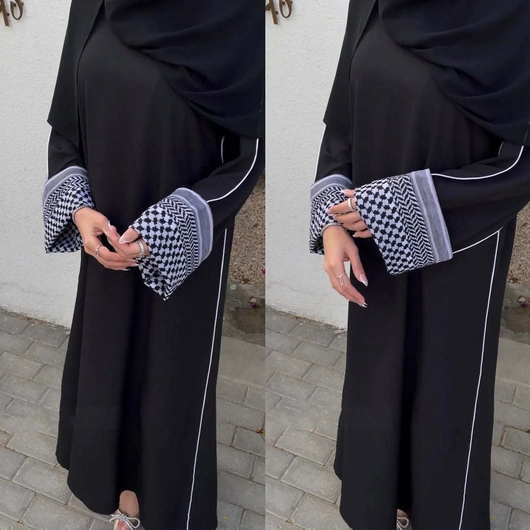 Woman wearing black abaya with white piping and patterned wide cuffs standing on pavement