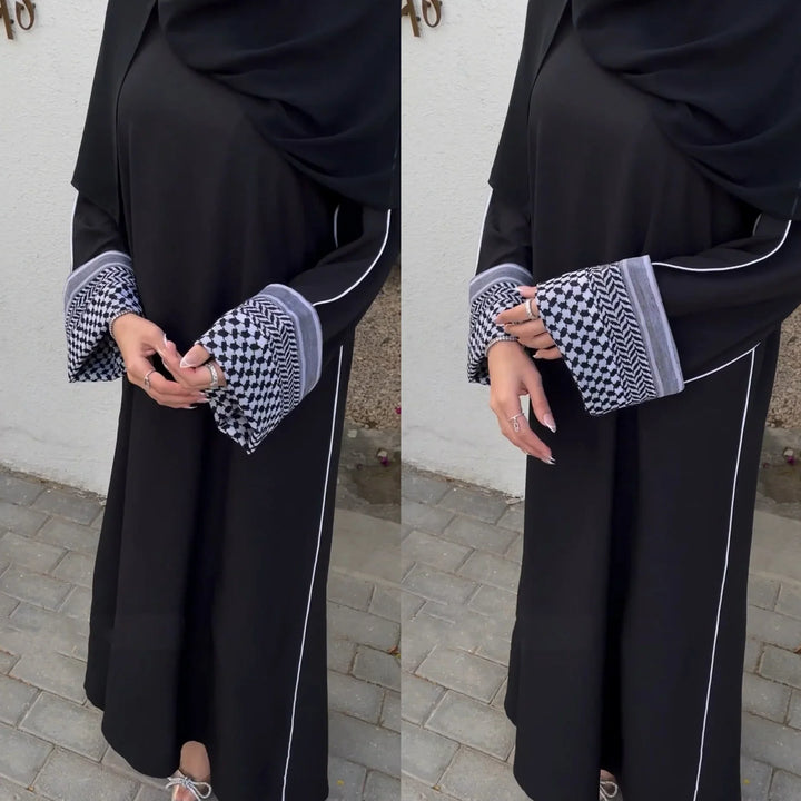 Woman wearing black abaya with white piping and patterned wide cuffs standing on pavement