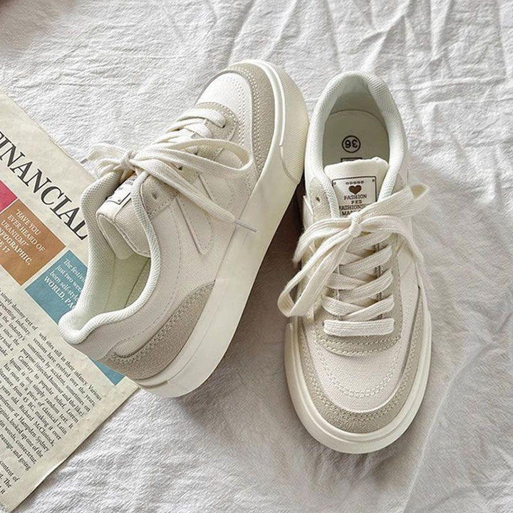 Pair of white and beige casual sneakers with laces on a light fabric surface next to a folded newspaper