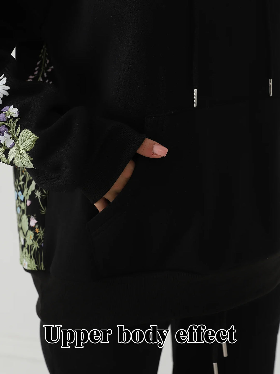 Close-up of a hand with pink nails in the pocket of a black hoodie with floral patterns on the sleeve