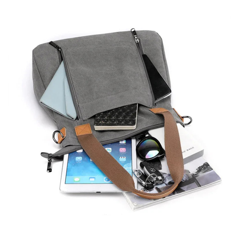 grey canvas tote bag with brown handles holding tablet, sunglasses, car keys, notebooks, and magazines