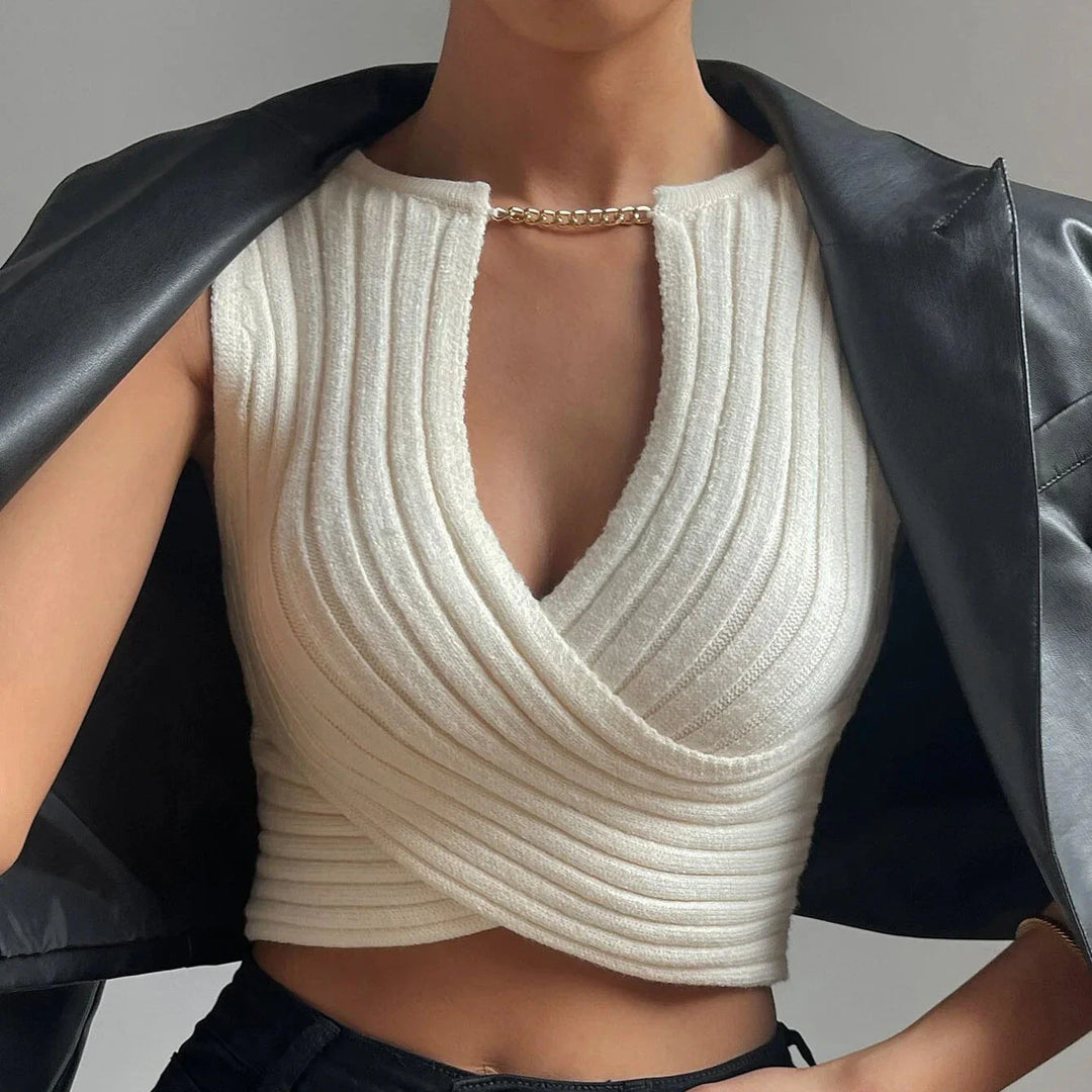 Woman wearing a white ribbed sleeveless knit crop top with gold chain detail, black leather jacket draped over shoulders