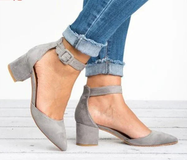 Woman wearing gray suede block heel ankle strap shoes with cuffed blue jeans on white wooden floor