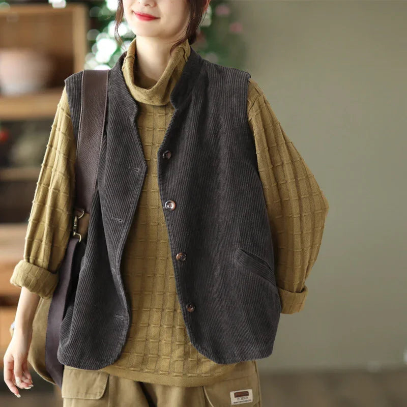 Woman wearing checkered beige turtleneck sweater and dark gray corduroy button vest indoors