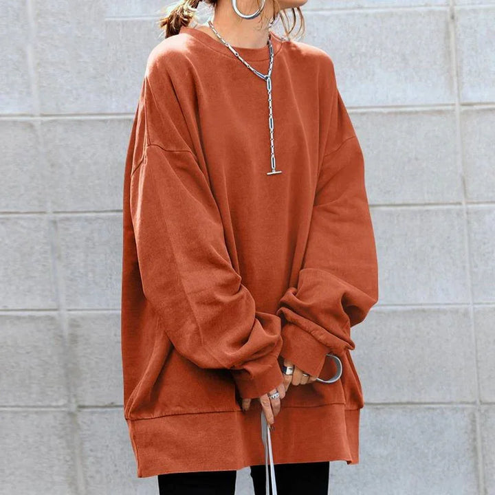 Person wearing oversized burnt orange sweatshirt with silver chain necklace, rings, and black pants