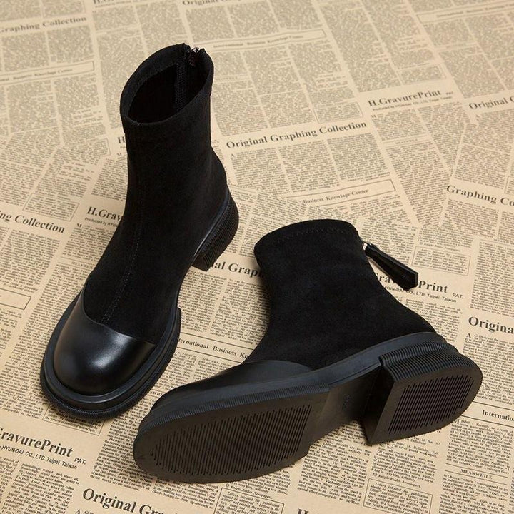 Black ankle boots with rubber soles and rear zipper on a newspaper print background