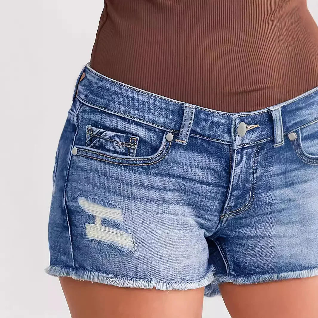 Close-up of distressed blue denim shorts with frayed edges worn with brown top