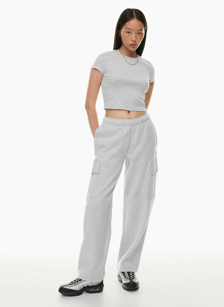 Woman in light grey crop top and cargo sweatpants with sneakers on white background