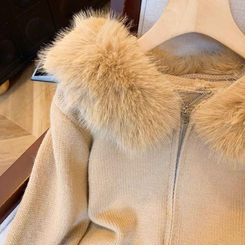 Beige knitted jacket with fluffy fur collar and front zipper hanging on wooden hanger