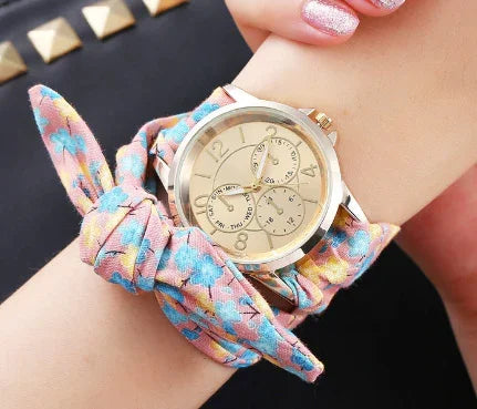 Gold-tone wristwatch with floral fabric wrap band on wrist, featuring multi-dial face and pink nail polish