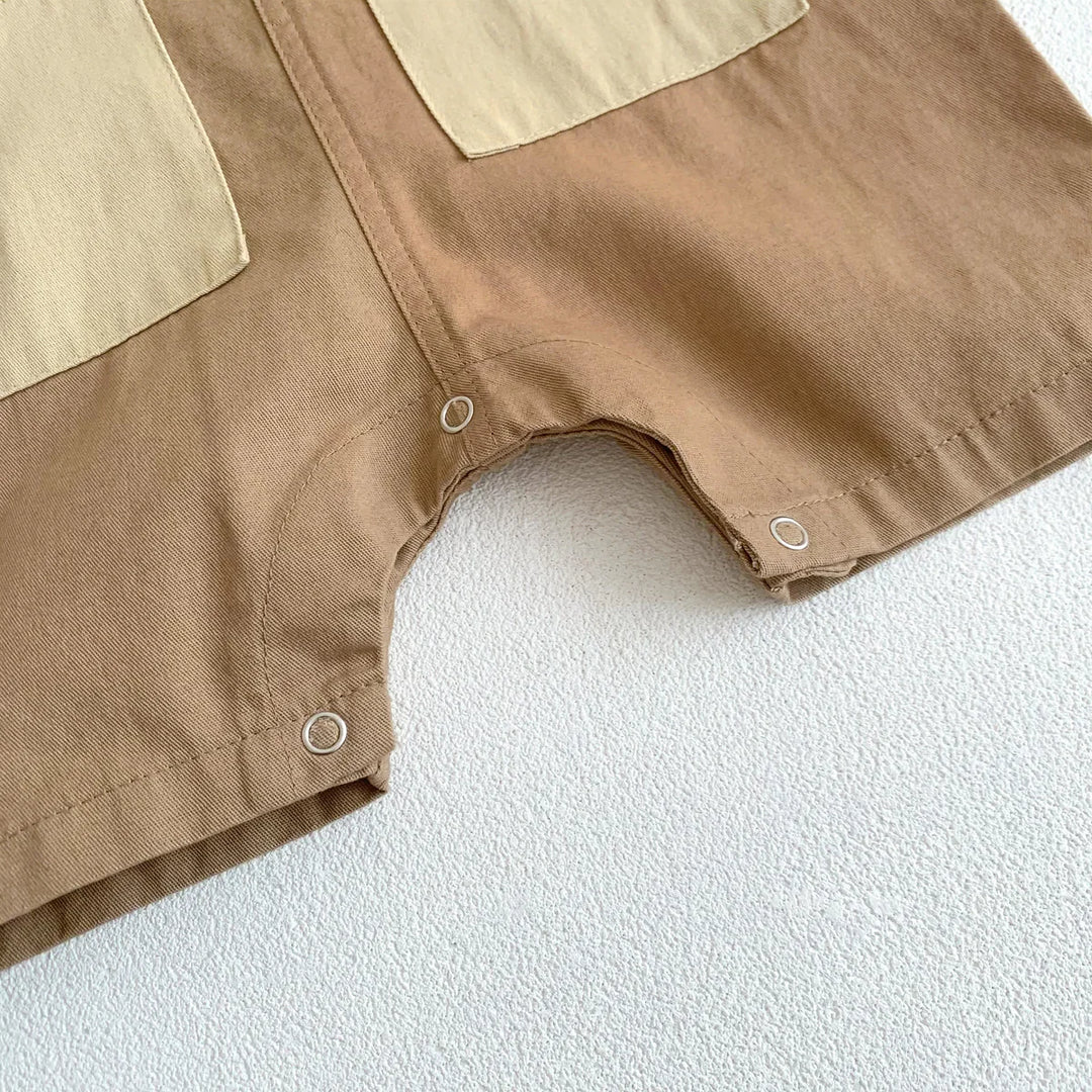 Close-up of brown baby romper with beige patch pockets and snap buttons on textured white surface