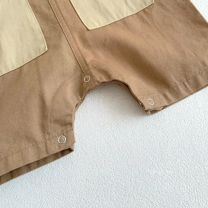 Close-up of brown baby romper with beige patch pockets and snap buttons on textured white surface