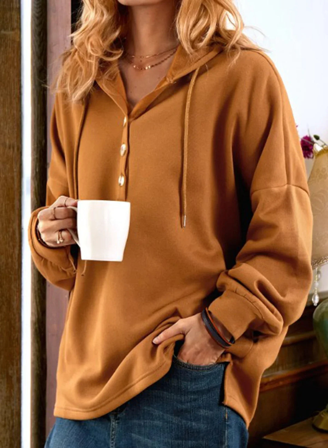 woman wearing a brown buttoned hoodie holding a white mug, casual fall fashion with blue jeans