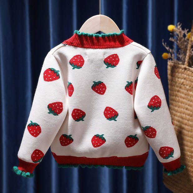 White knit sweater with red and green strawberry pattern, red collar and cuffs with green trim, hanging on wooden hanger