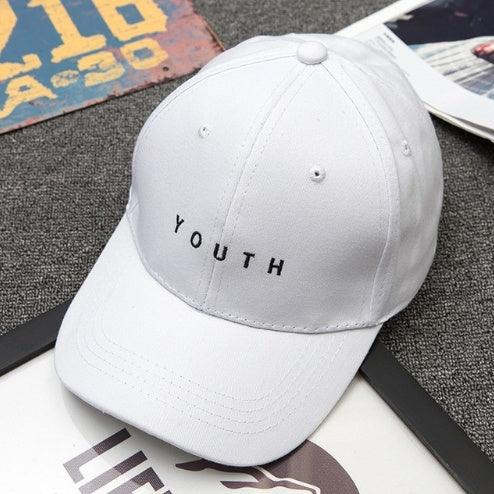 White baseball cap with YOUTH embroidered in black, placed on gray carpet with magazines nearby