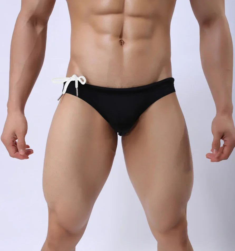 Muscular man wearing black swim briefs with white side tie against plain background