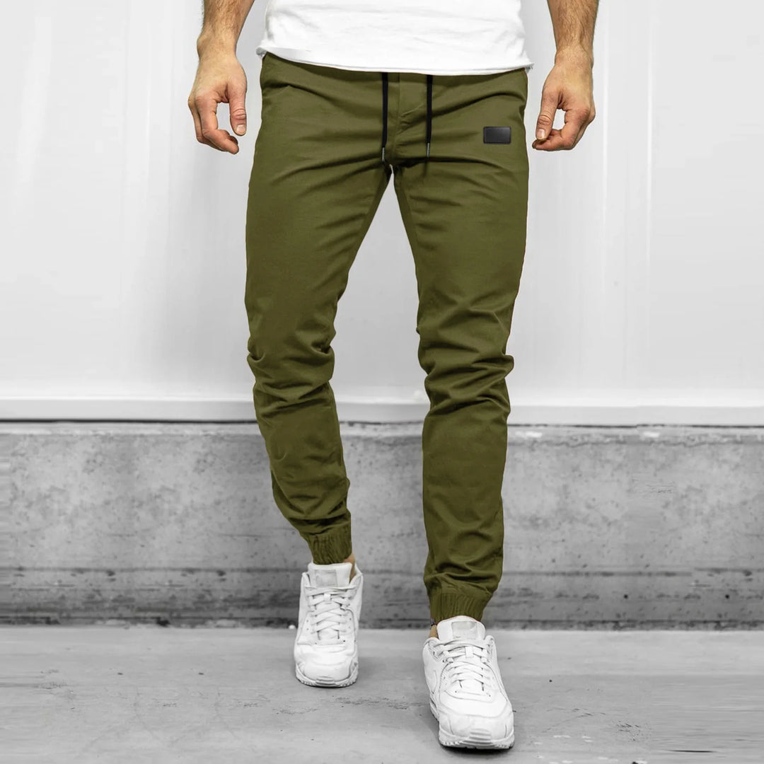 Man wearing olive green jogger pants with black drawstring and white sneakers in urban setting