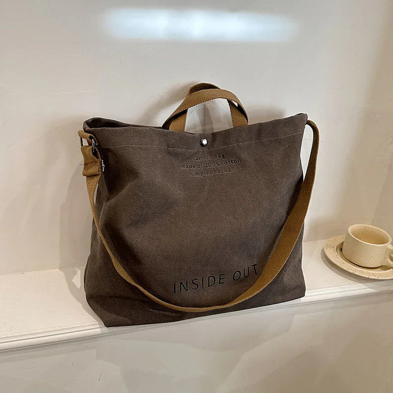 brown canvas tote bag with adjustable strap and text inside out on white shelf next to cup and saucer