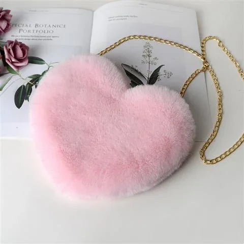 Pink fluffy heart-shaped purse with gold chain on botanical book background