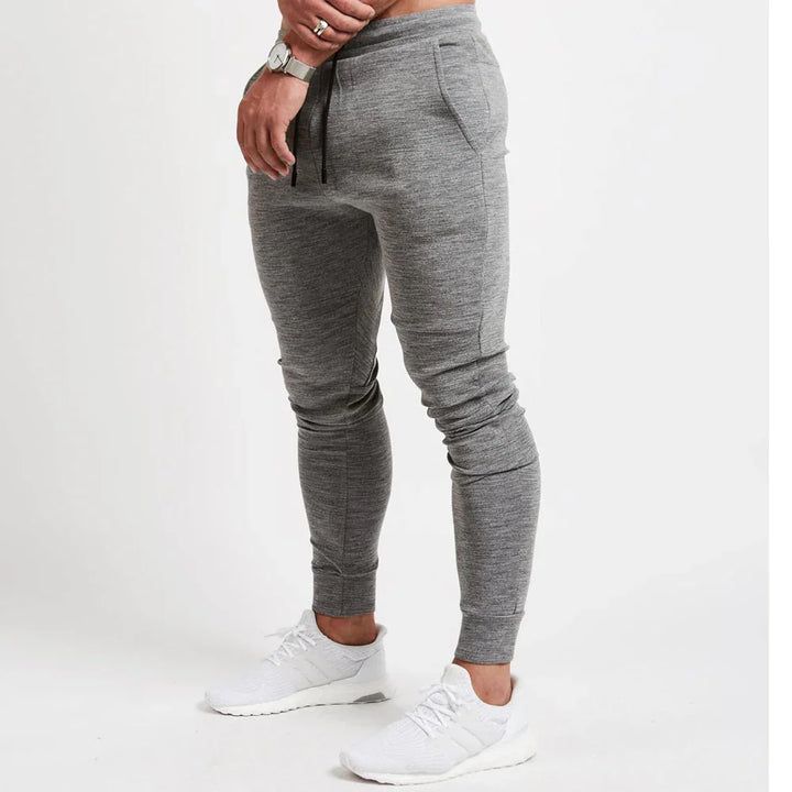 Man wearing slim fit grey jogger pants with front pockets and white sneakers on white background