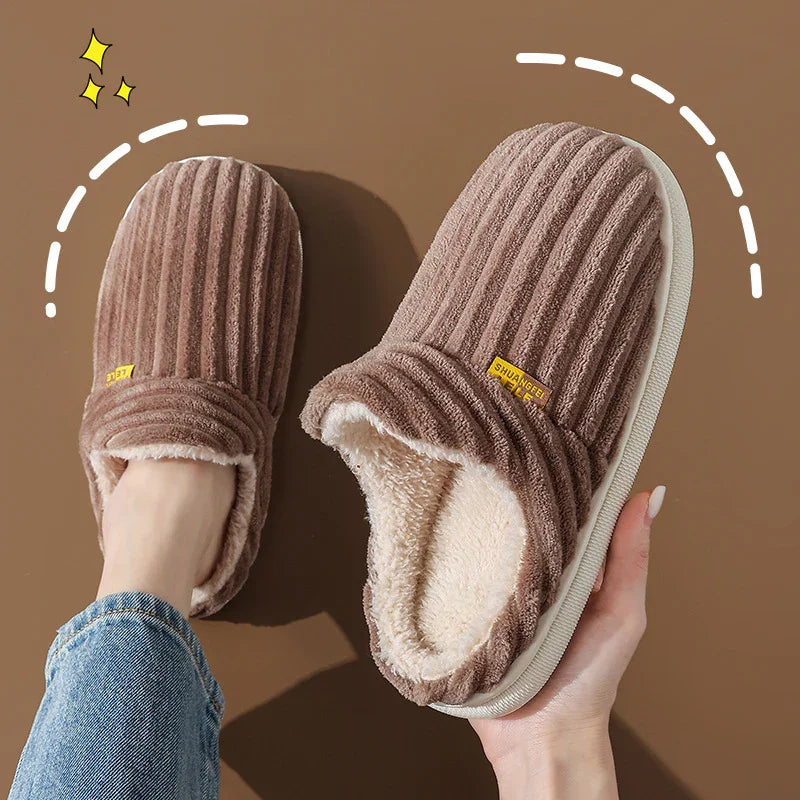 Brown cozy fleece-lined slippers with ribbed texture, one worn and one held by hand