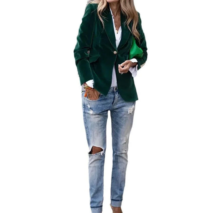 Woman wearing a dark green velvet blazer over white shirt and ripped light-wash jeans holding a green clutch