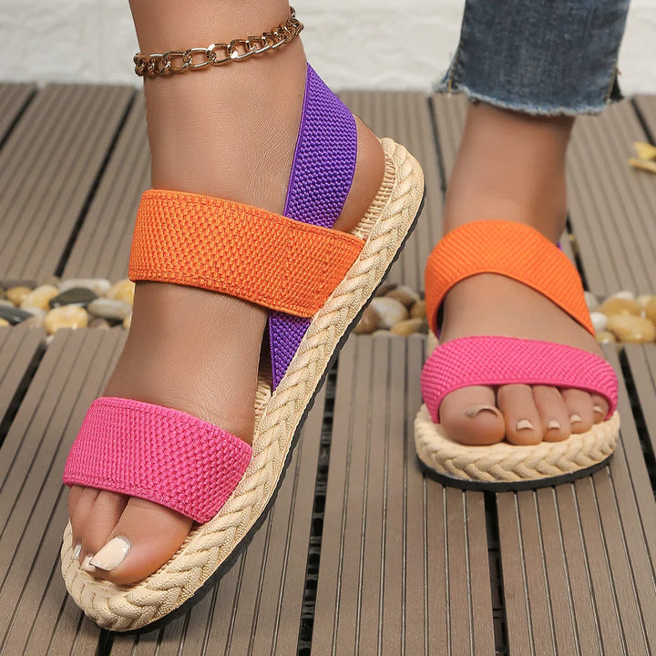 Close-up of feet wearing colorful sandals with orange, purple, and pink straps on wooden deck