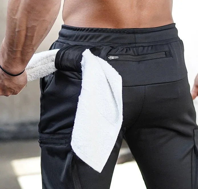 Athletic man wearing black workout joggers with zip pocket and white towel tucked in waistband
