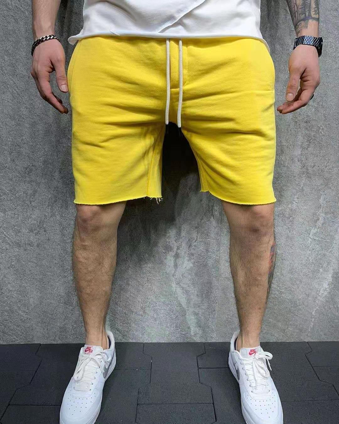Man wearing bright yellow casual shorts and white Nike sneakers against gray textured wall
