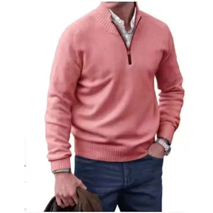 Man wearing pink quarter-zip sweater over white shirt with blue jeans, holding jacket in hand