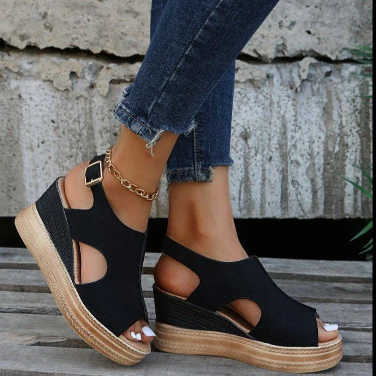 Women's casual black wedge sandals with cutouts and ankle buckle, paired with cropped blue jeans and gold anklet