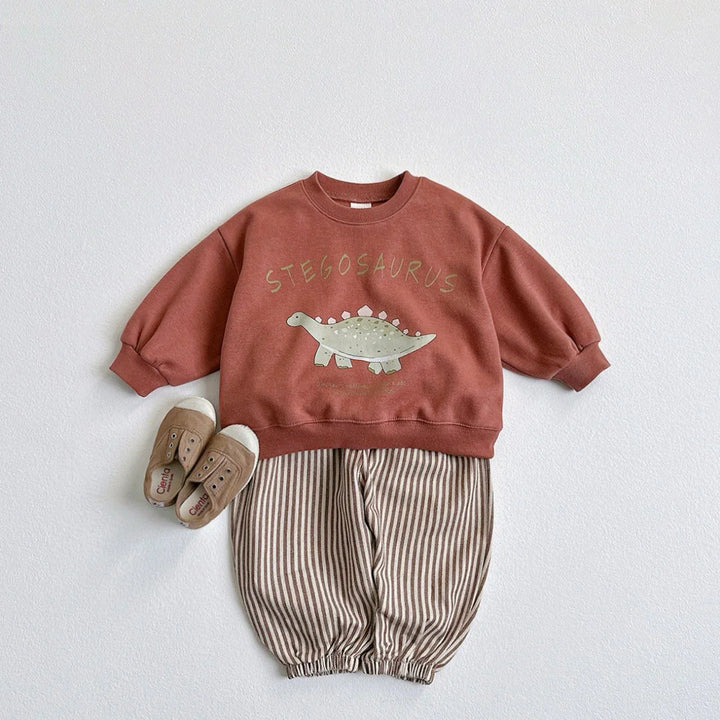 Kids outfit with rust-colored stegosaurus sweatshirt, striped pants, and beige slip-on shoes