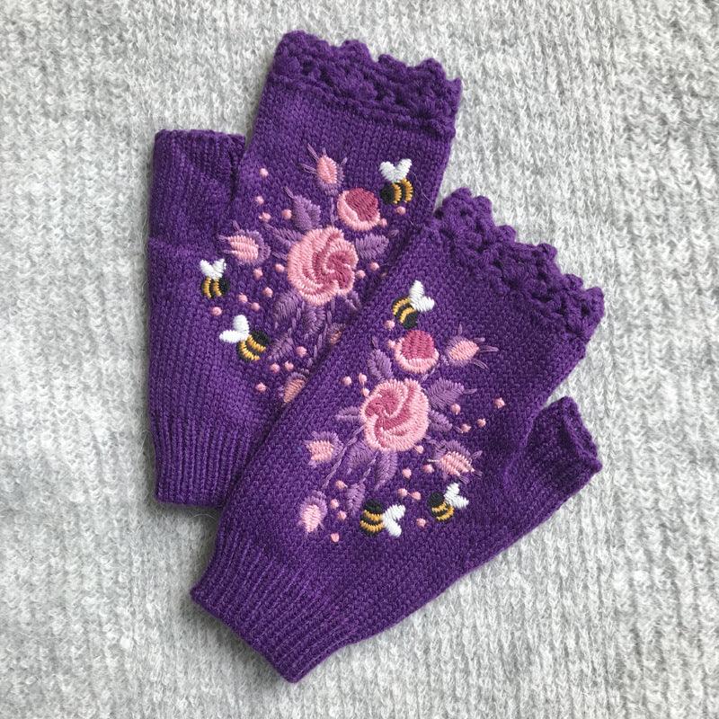 Purple fingerless gloves with pink floral embroidery and small bees on gray knitted background