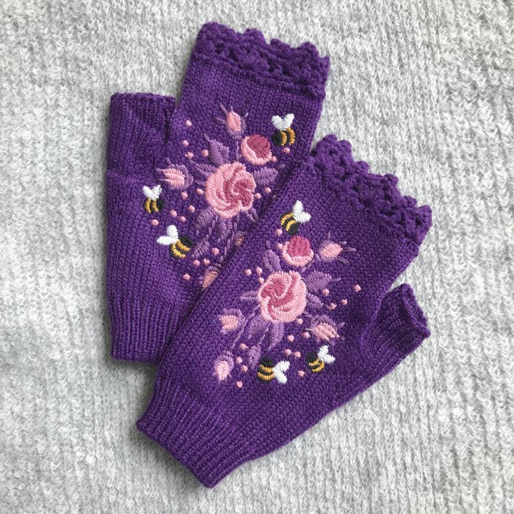 Purple fingerless gloves with pink floral embroidery and small bees on gray knitted background