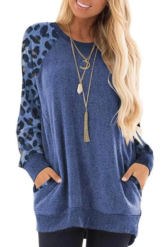 Woman wearing blue long-sleeve leopard print sleeve sweatshirt with front pockets and layered necklaces