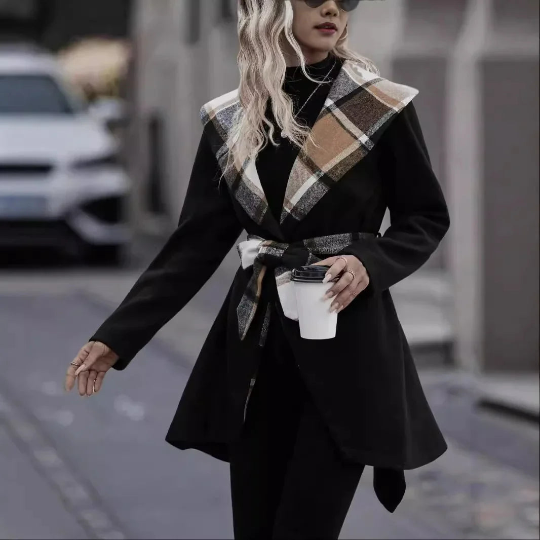Woman in black coat with large plaid collar and belt holding white coffee cup on city street