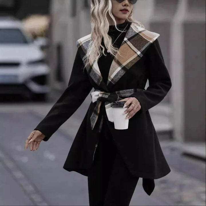 Woman in black coat with large plaid collar and belt holding white coffee cup on city street