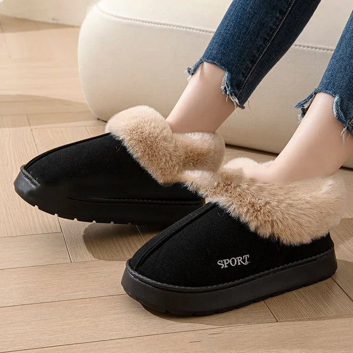 Black slip-on indoor slippers with beige faux fur lining worn with frayed hem jeans on wooden floor