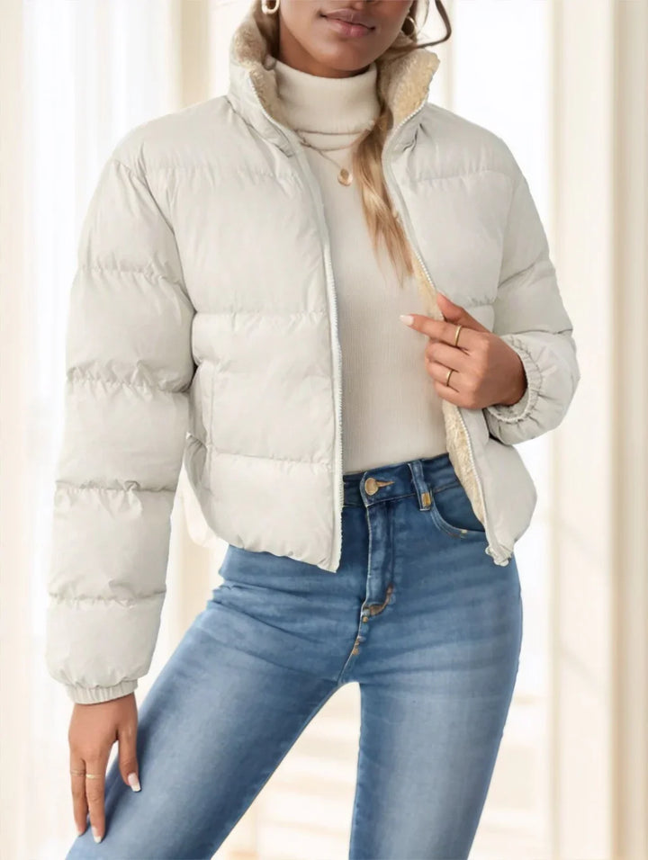 Woman wearing light beige puffer jacket with shearling lining, cream turtleneck sweater, and blue jeans