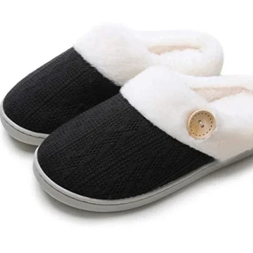 Black cozy knit slippers with white plush lining and wooden button detail on gray sole