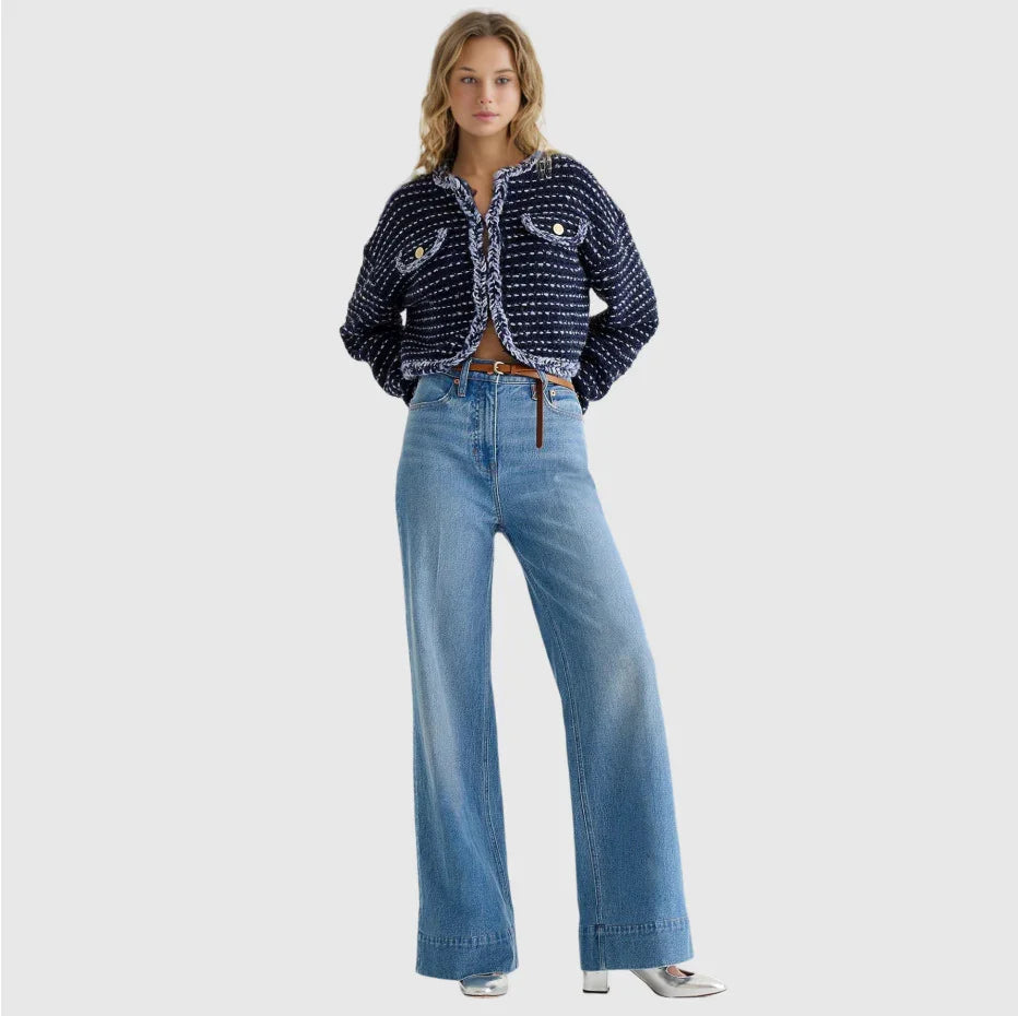 Woman wearing navy textured cropped jacket with white trim and wide-leg blue jeans